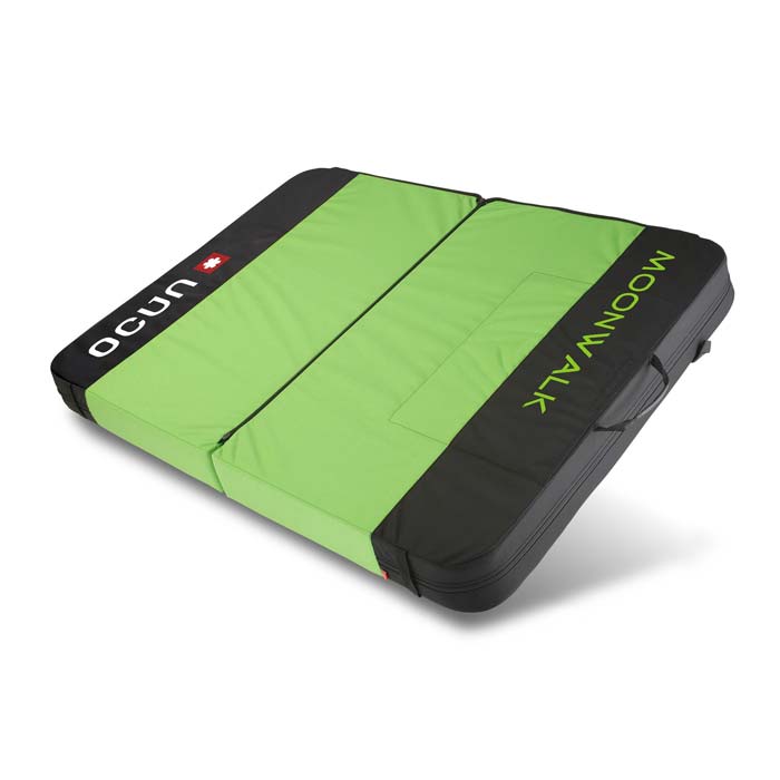 Das Bild zeigt die Ocun Moonwalk Bouldermatte. Sie liegt ganz aufgeklappt schräg im Bild. Man erkennt das Crashpad mit all seinen Features wie Trageriemen, grüne Oberseite und robuste Unterseite aus schwarzem Balistic Cordura sehr gut.