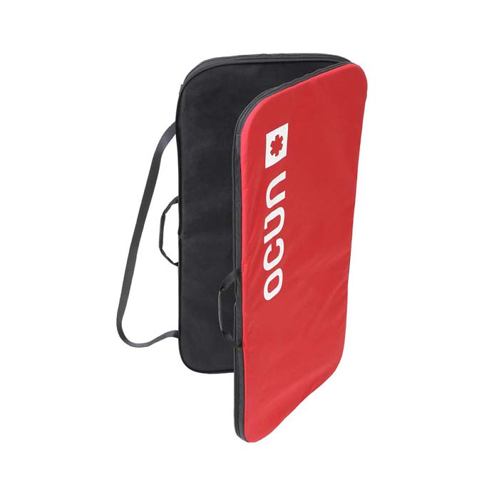 Das Bild zeigt die Ocun Sitcase Bouldermatte. Das Crashpad steht leicht aufgeklappt in Bildmitte. Man erkennt die schwrze Innenseite, die zwei Trageriemen, den Schulterriemen und die rote Außenseite mit dem Logo.