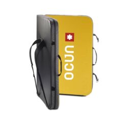 Das Bild zeigt die Ocun Sundance Bouldermatte. Das Pad steht leicht aufgeklappt in Bildmitte. Man erkennt die gelbe Innenseite, die zwei Trageriemen, den Schulterriemen und die schwarze Außenseite mit dem Logo.