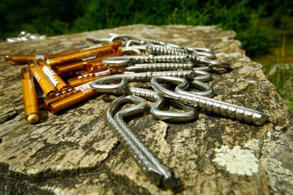 Das Bild zeigt einige silberne Klebehaken und braune Glasmörtelpatronen als Beipsiel für Einbohrartikel auf einer grauen Felsplatte.